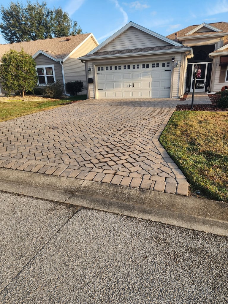 Single-story home with gray garage door and paver driveway before restoration
