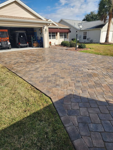 Paved driveway in front of a single-story house with open garage, green lawn, and palm tree in Florida