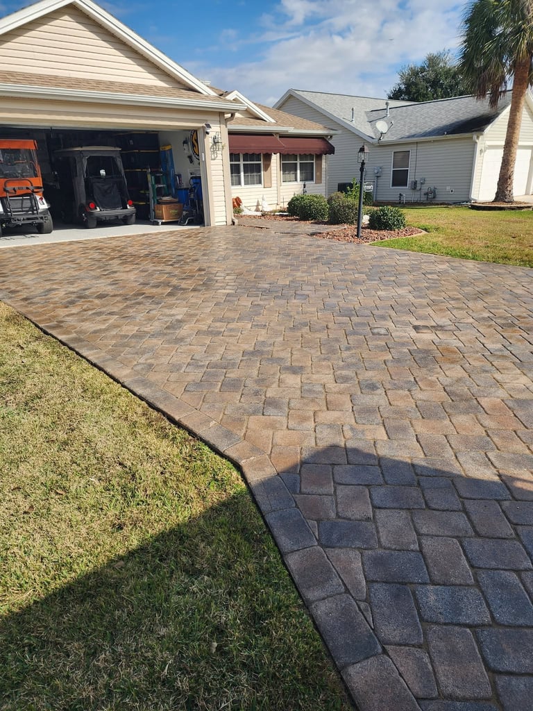 Residential home with brick paver driveway, open garage, and manicured lawn on a sunny day