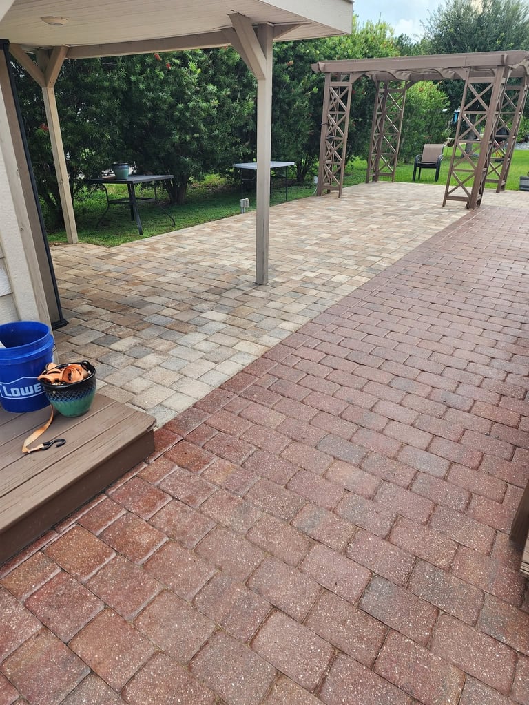 Spacious outdoor patio with brick pavers, wooden pergolas, and green lawn in background