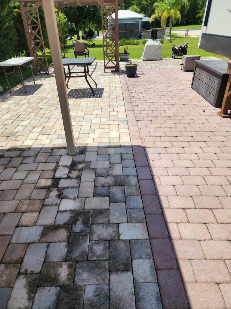 Patio area with brick pavers showing a wet, moss-covered section transitioning to clean areas, with pergola, outdoor furniture, and green yard visible