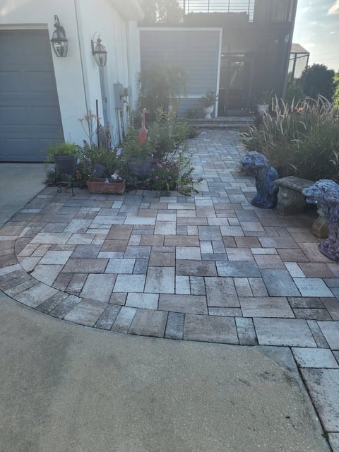 Paved driveway with herringbone pattern pavers leading to a house garage and front entrance with decorative plants and landscaping