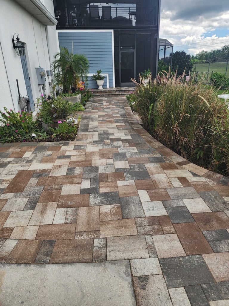 Patterned brick patio leading to a modern black and white home with landscaped plants and ornamental grasses on either side